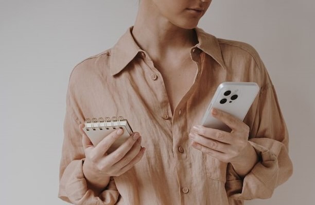 Woman using phone and notebook for trading